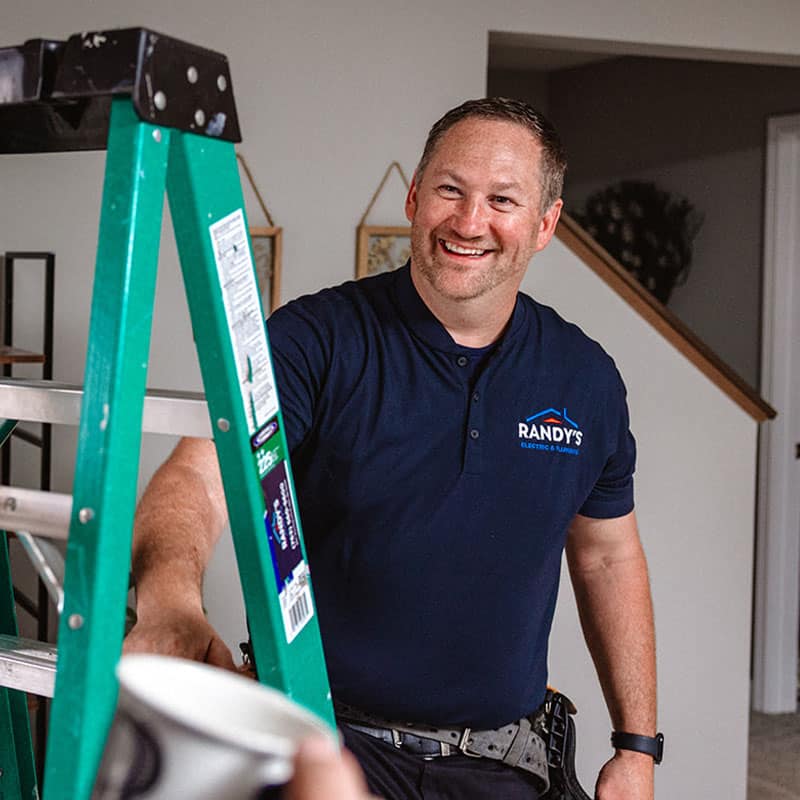 Man in a Summmit Electric shirt smiling by a green ladder indoors.