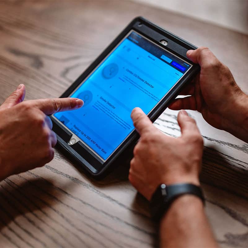 Hands using a tablet on a wooden table, navigating a website.