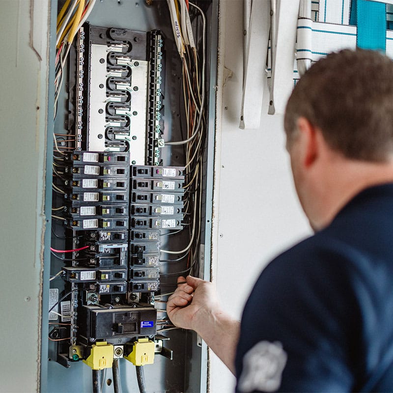 Electrician working on a circuit breaker panel, connecting wires for electrical maintenance.