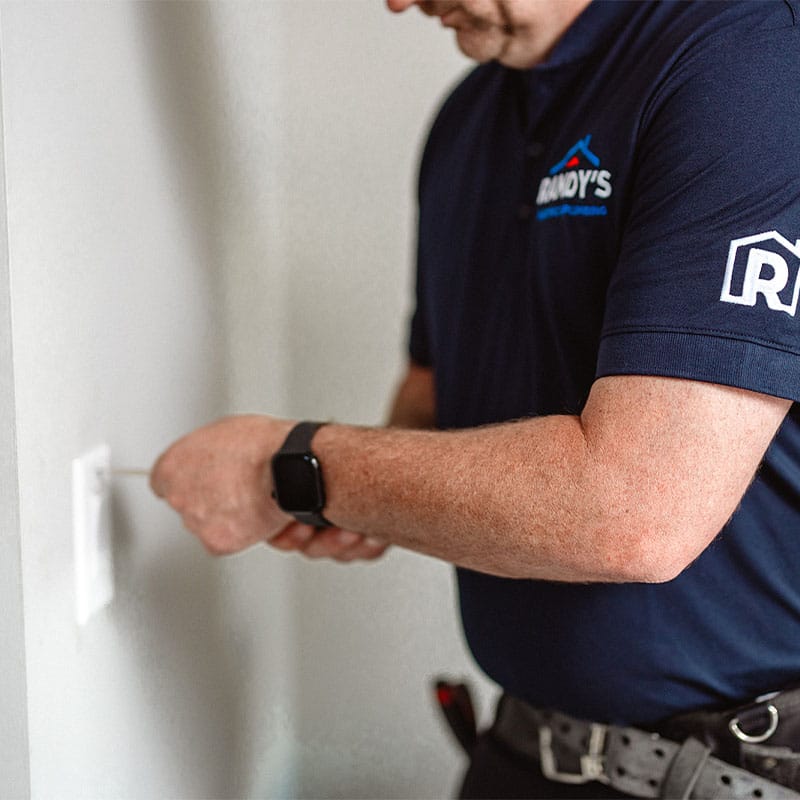 Person fixing wall outlet wearing Summmit Home Services shirt.