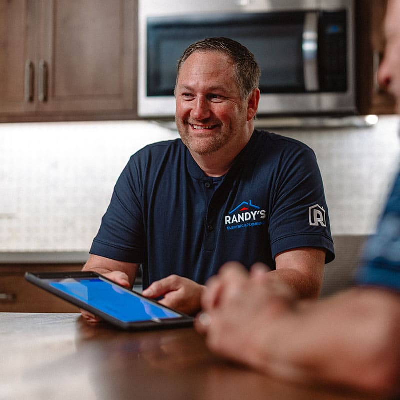 A man in a Summit Electric & Plumbing shirt holding a tablet, smiling at a table.