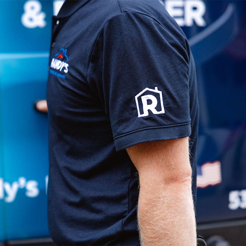 Person wearing navy shirt with R logo, standing near a blue vehicle.