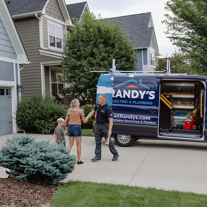 Electrician from Summit Electric & Plumbing greeting a woman and child in front of a house.