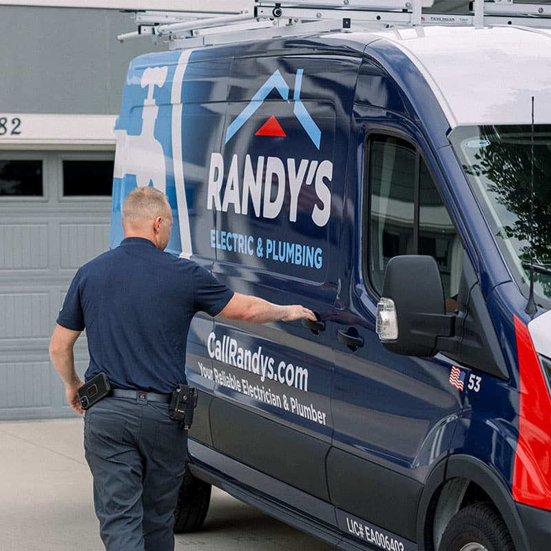 A man opening a Summit Electric & Plumbing van near a garage.