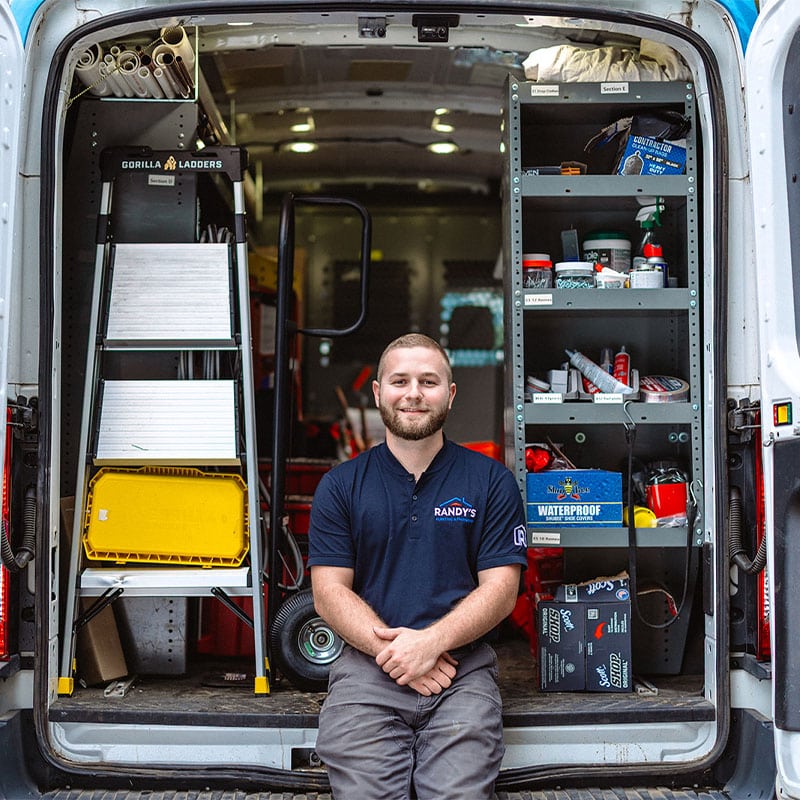 A man in a Summmit uniform sits in the back of a work van with shelves and equipment.