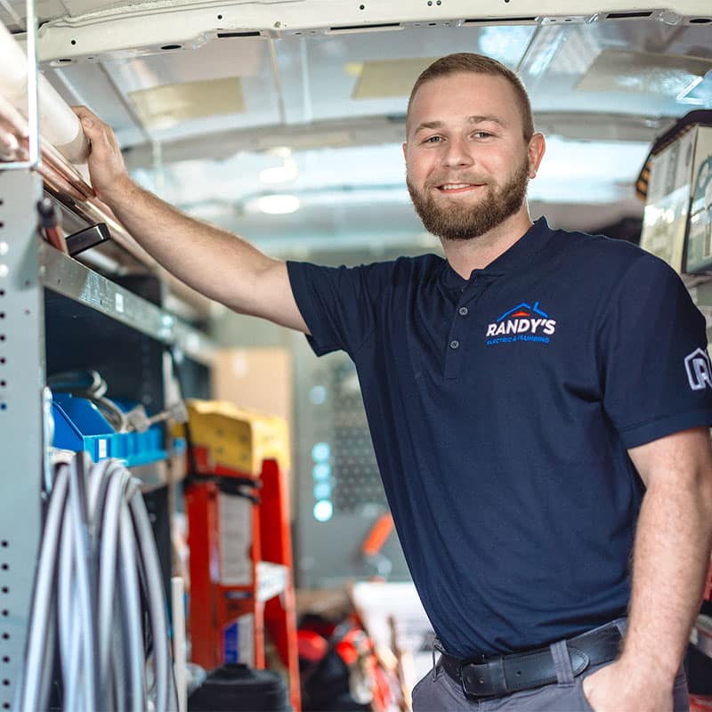 Man smiling inside a work van, wearing a Summmit Plumbing shirt.