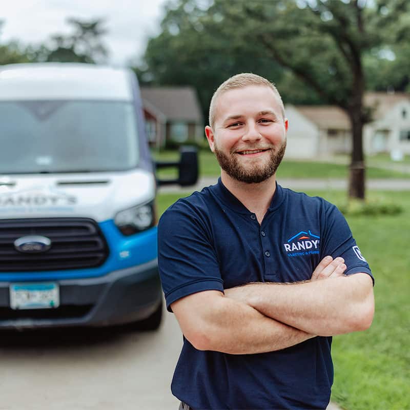 A man in a Summmit Electric shirt stands smiling in front of a branded service van on a residential street.