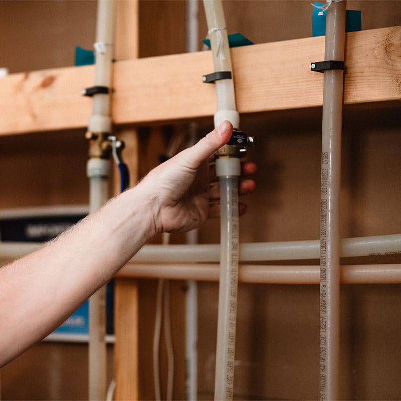 A person's hand adjusting a pipe valve in a wooden frame, focusing on plumbing maintenance.