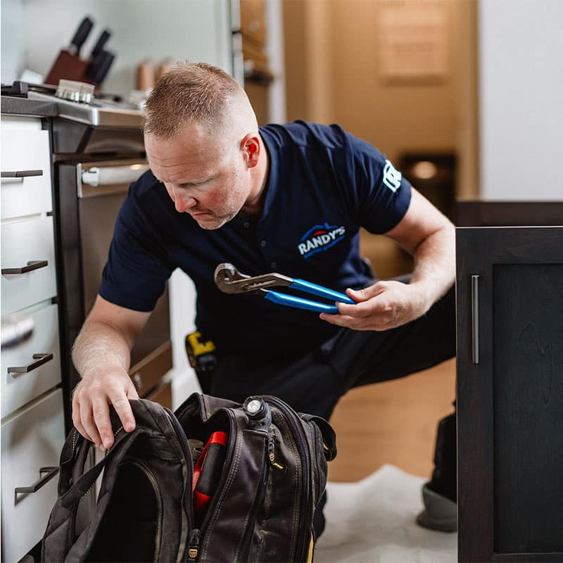 A plumber checking tools in a kitchen, wearing a Summmit uniform and holding a wrench.