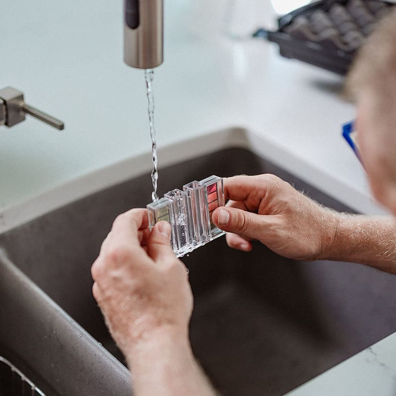 Person rinsing a clear plastic object under a faucet at a sink.