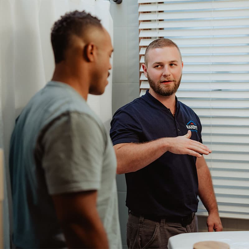 Two men discussing a home repair project in a bathroom setting.