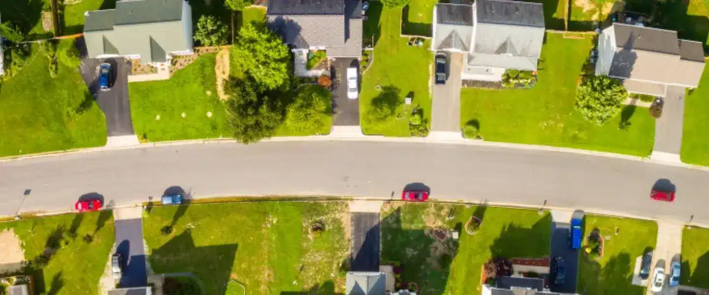 Aerial view of suburban neighborhood with houses and parked cars along a curving road.