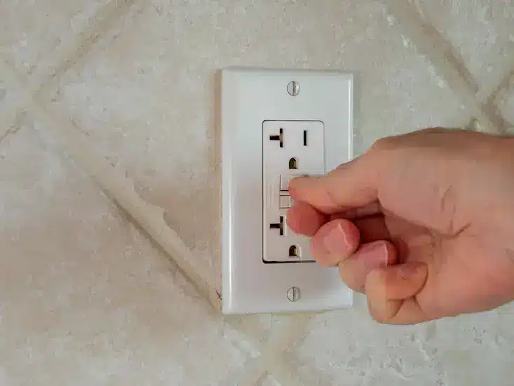 Hand resetting a GFCI outlet on a tiled wall for safety and electrical checks.