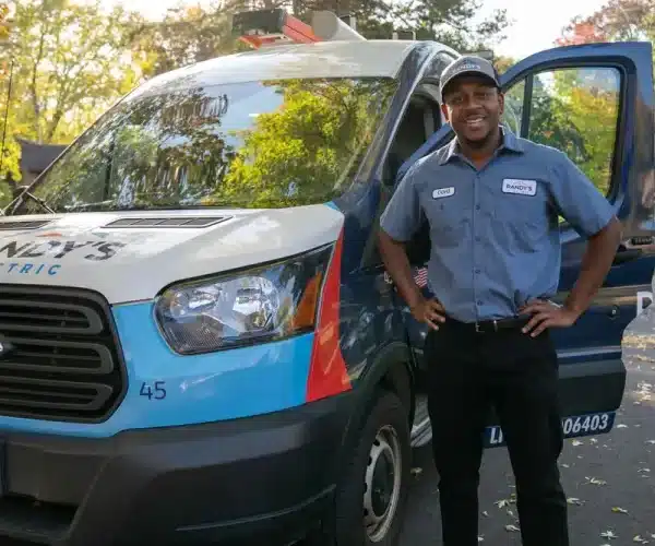 Connor standing next to Summmit Electric van with open door, wearing uniform and cap.