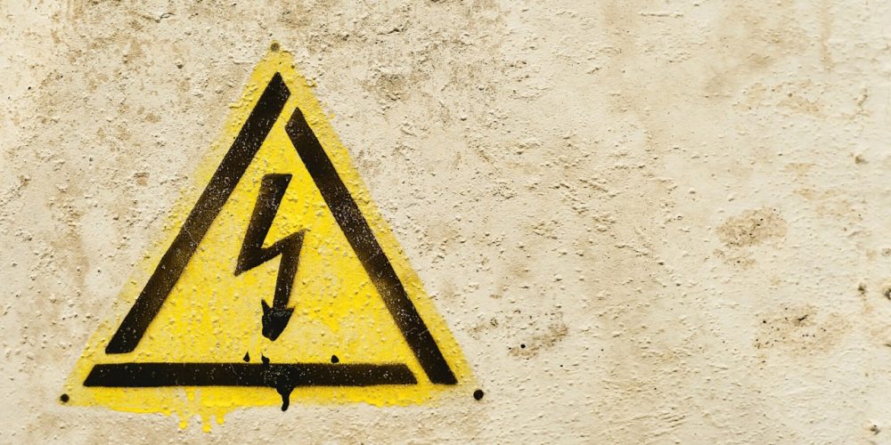 Yellow high voltage warning sign on textured wall background.