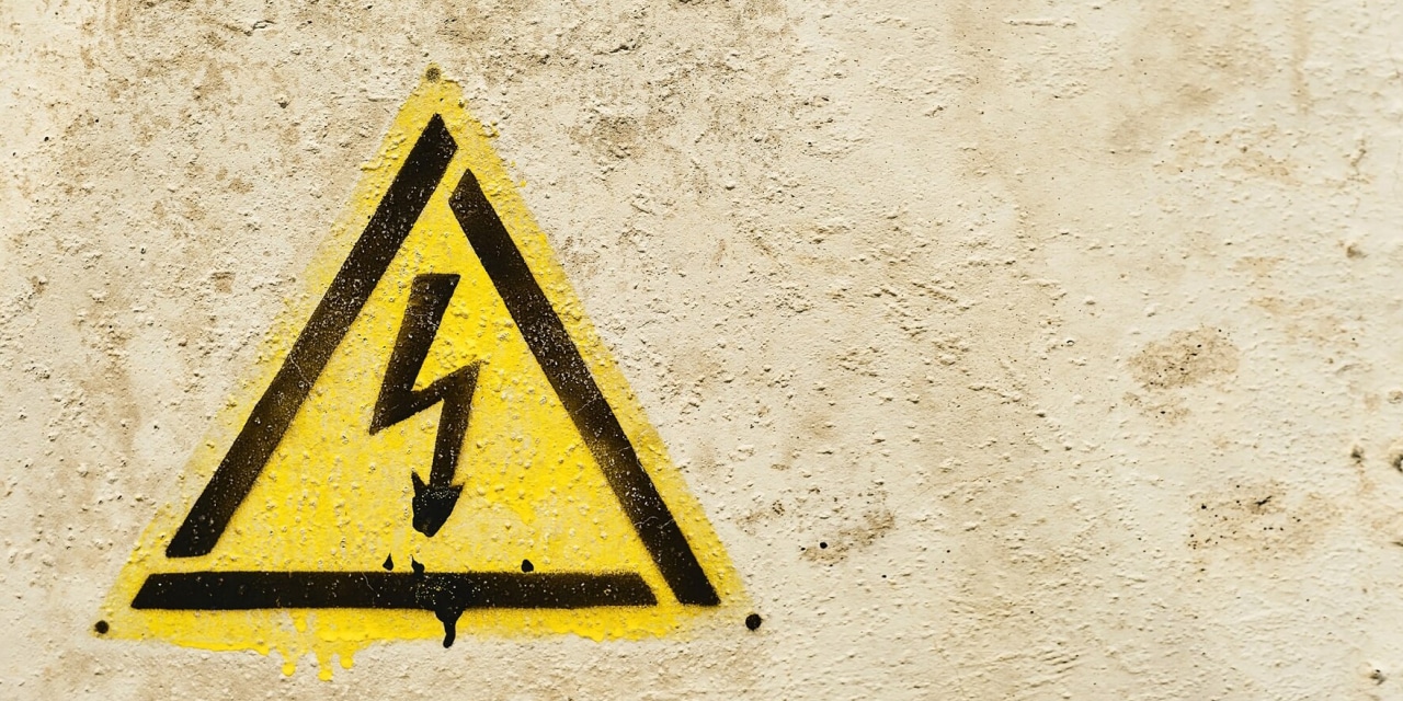 Yellow high voltage warning sign on textured wall background.
