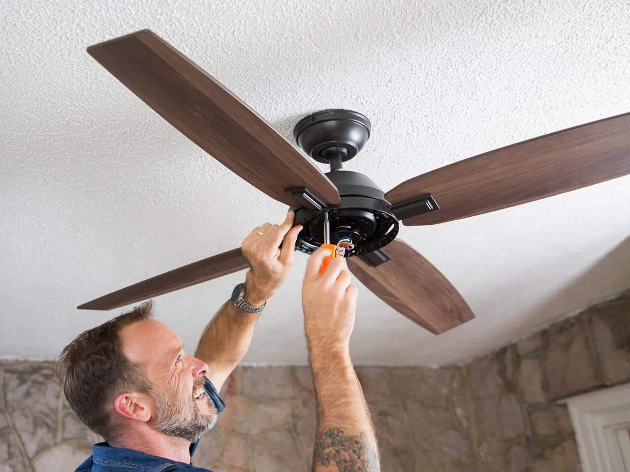 Man installing a wooden ceiling fan with a screwdriver indoors.