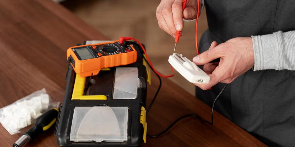 Person testing electrical device with multimeter on table with tools.