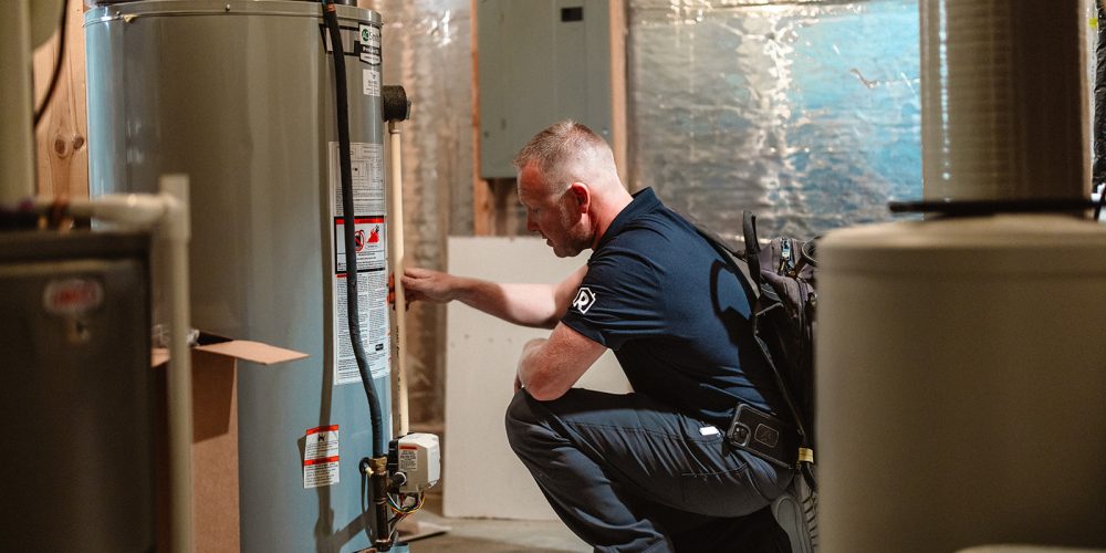 A licensed plumber from Summit Electric & Plumbing inspecting a water heater inside the basement of a Tennessee home.