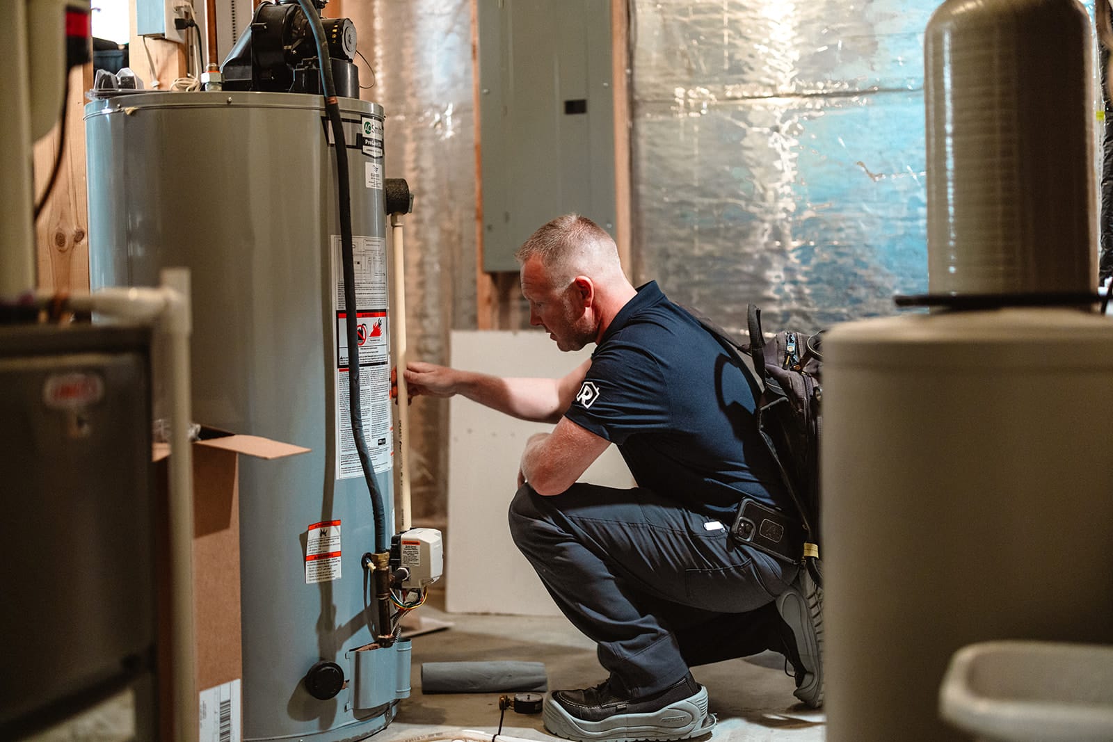 A licensed plumber from Summit Electric & Plumbing inspecting a water heater inside the basement of a Tennessee home.