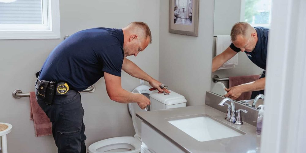 A plumber from Summit Electric & Plumbing performing repairs on a toilet.
