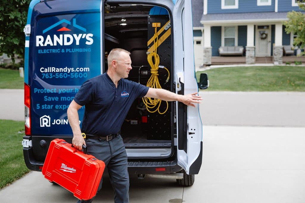 Service technician with red toolbox at Summit Electric & Plumbing van outside a home, closing door before service call.