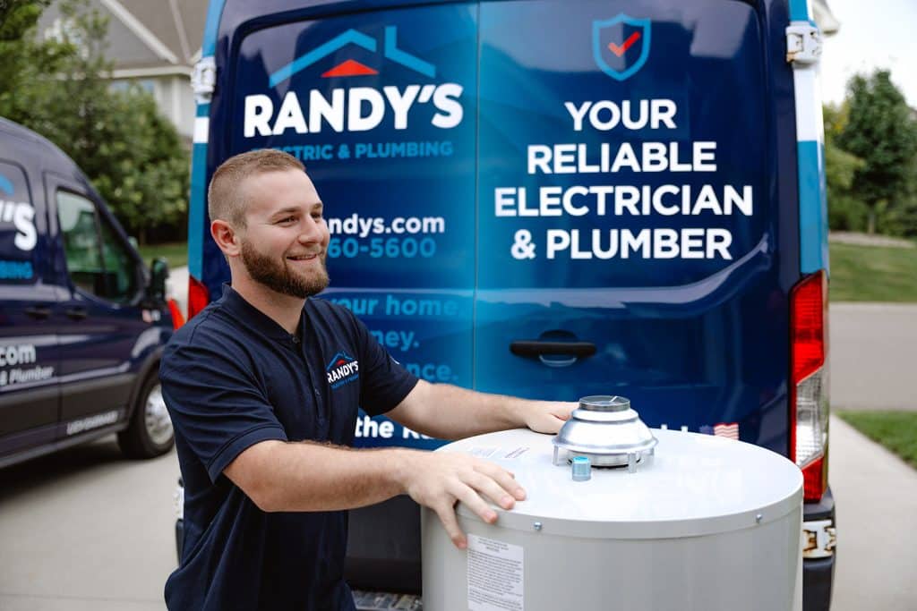 Smiling technician installs water heater beside Summit Electric & Plumbing service van in a residential driveway