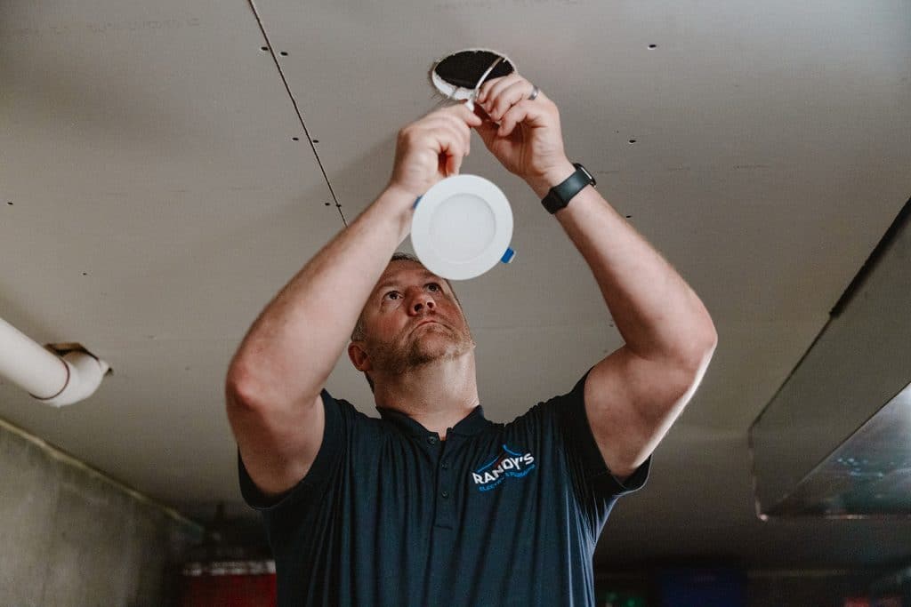 A electrician from Summmit installing a recessed LED ceiling light fixture in a basement ceiling