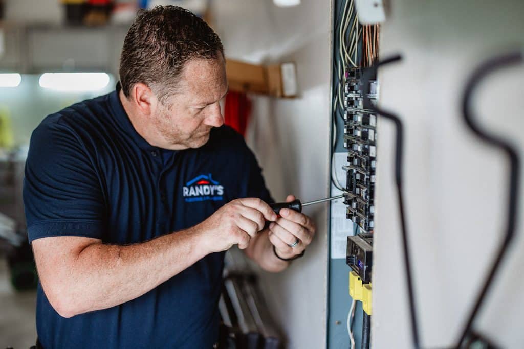 Electrician repairing a home circuit breaker panel with a screwdriver — professional electrical service and safety.